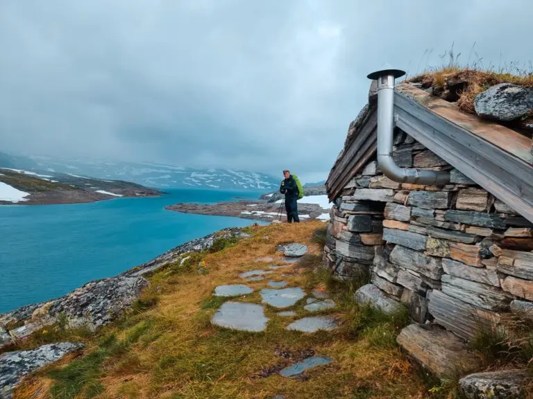 hiker with backpack and trekking poles by stone hut in Norway