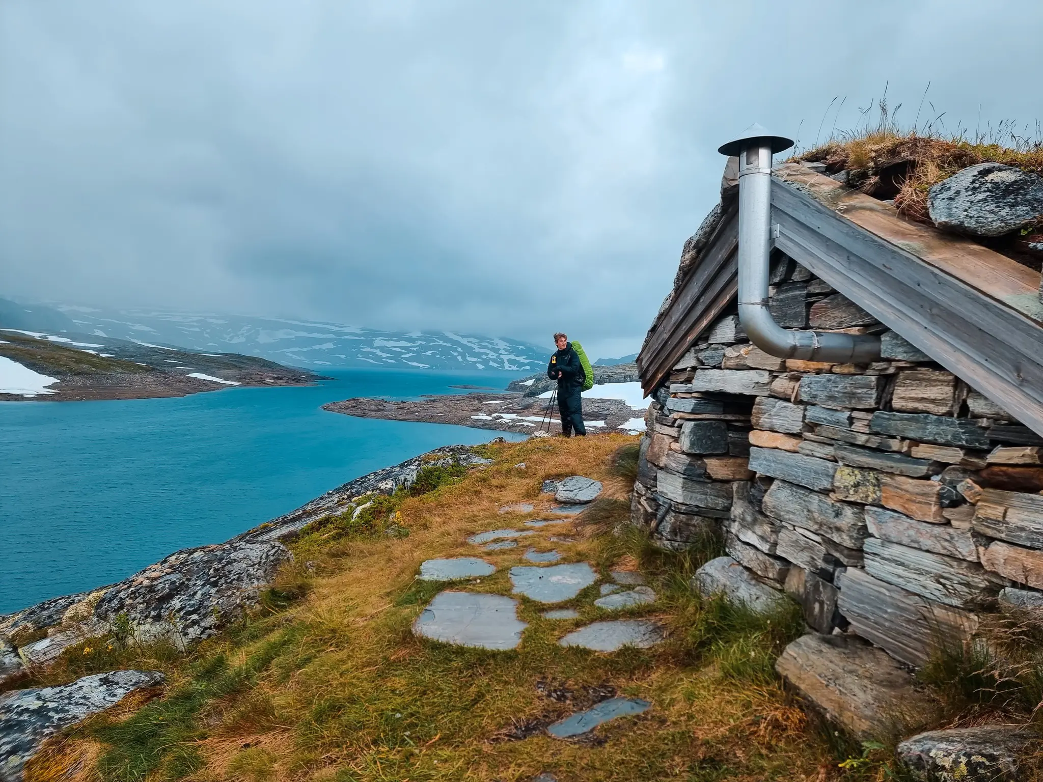 hiker with backpack and trekking poles by stone hut in Norway