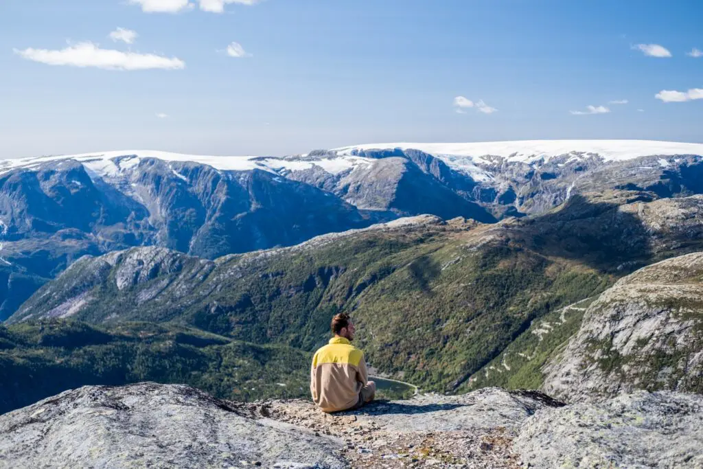 man sitting on mountain edge overlooking snowy peaks and valley