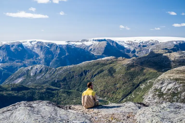 man sitting on mountain edge overlooking snowy peaks and valley