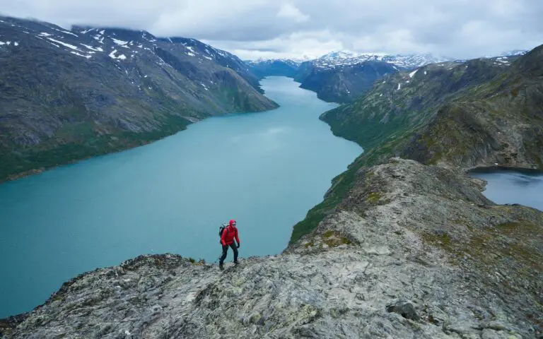 a man standing on top of a mountain next to a lake